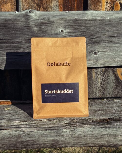 Startskuddet-posa står mot en gammel fjøsvegg. Marineblå etikett på kraftpapir.